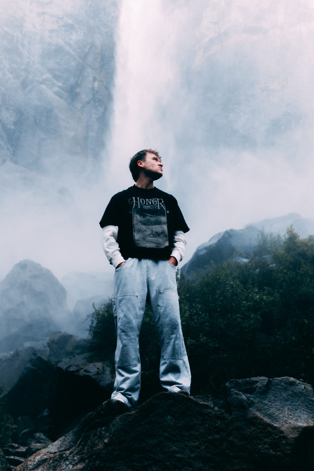 Hagan Compton standing on a boulder in front of a misty waterfall