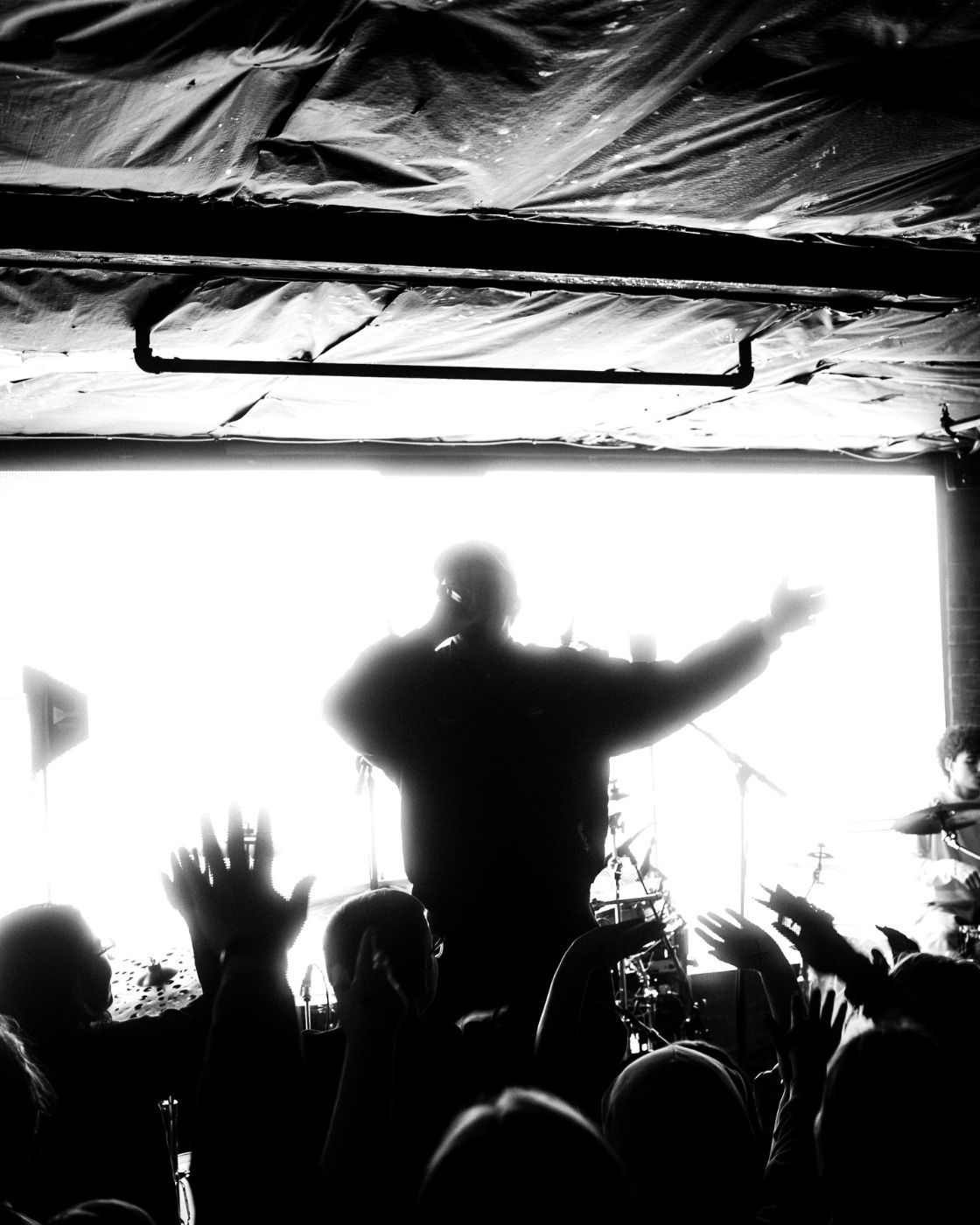 Silhouette of Jude Barclay on stage, arm raised over a cheering crowd, in black and white
